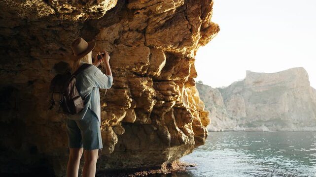 Female traveler with backpack using vintage camera to photograph sunrise by sea, embracing slow travel and enjoy authentic outdoor experience.slow travel, mindful travel, authentic experience concept