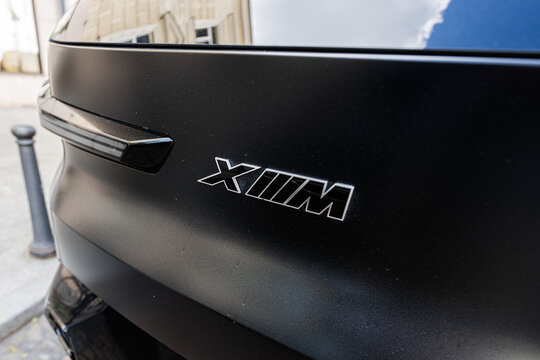 Close-up of black car emblem BMW XM on rear panel with chrome lettering and matte finish urban street scene