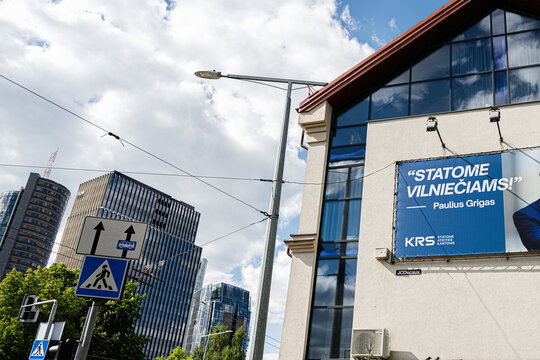 Political billboard campaign for Paulius Grigas on a modern building facade in Vilnius, Lithuania with city skyline and pedestrian crossing