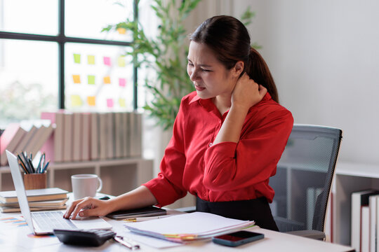 Woman experiencing neck and shoulder pain from long hours at the computer, massaging her stiff muscles due to office syndrome-related stress and fatigue
