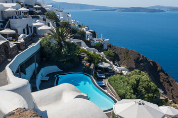 Luxury infinity pool with whitewashed buildings on a Santorini cliff above the Aegean Sea on a sunny day. © Andrei Tomas