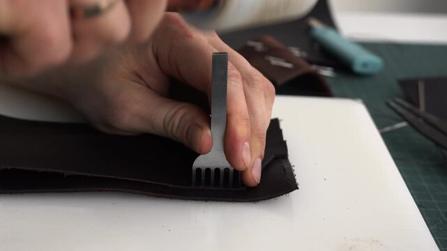 Leatherworker punching stitching holes in genuine leather with a mallet and pricking iron for a handmade product