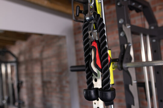 Black twisted tricep rope is hanging from metal carabiner on yellow support, with red strap visible