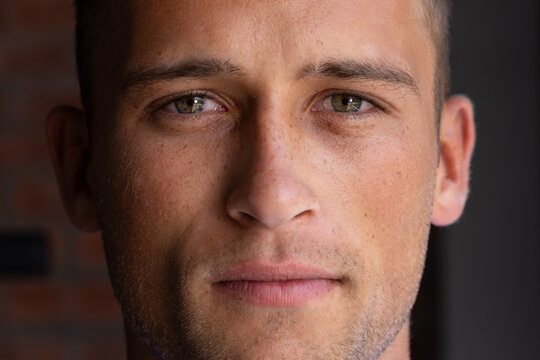 Adult male looking directly at camera in room, filling frame with freckled face and brick wall