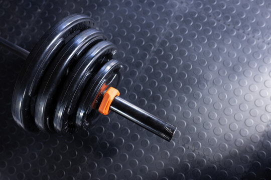 Barbell end is resting on textured rubber gym floor, orange collar securing stacked black plates