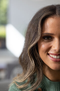 Female smiling and showing teeth, posing at home with long wavy hair wearing green ribbed sweater