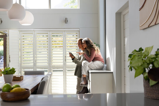 Diverse couple using handheld device, sitting on countertop in kitchen with fruit, copy space