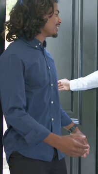 Vertical video: Stepping visitor in navy shirt entering foyer as host inviting, opening black door