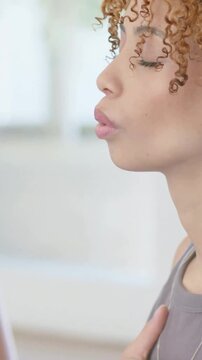 Vertical video: Placing right-hand on chest, woman taking calm breaths by window, grey top necklace