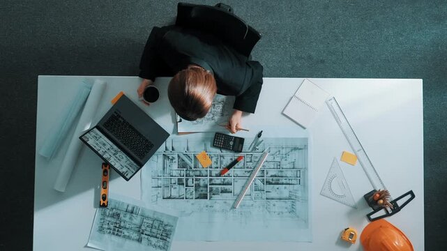 Top view of architect engineer drink coffee and draw blueprint at meeting table with equipment and safety helmet scatter around. Aerial view of project manager looking at project plan. Alimentation.