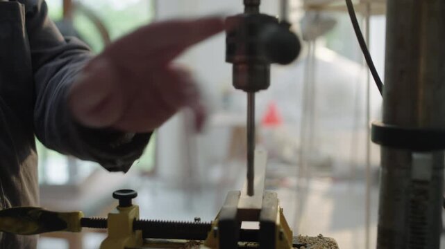 Craftsman drills wood in workshop vise during carpentry and woodworking process in bright workshop
