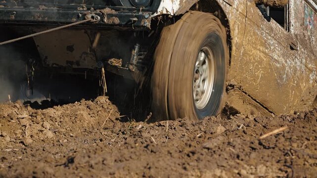 Action close up of 4x4 car wheel driving through thick mud. Tire spins fast, splashing dirt during extreme motorsport event. Dynamic view of rugged vehicle in dirty offroad challenge