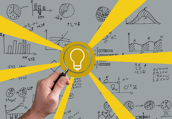 Magnifying glass highlights a light bulb among business charts for data insight.