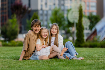 Fototapeta premium three children sitting on a lawn in the summer, in front of a residential complex in a city park