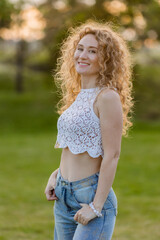 Fototapeta premium portrait of a young beautiful woman with curly blonde hair. smiling, looking at the frame in the summer in the park