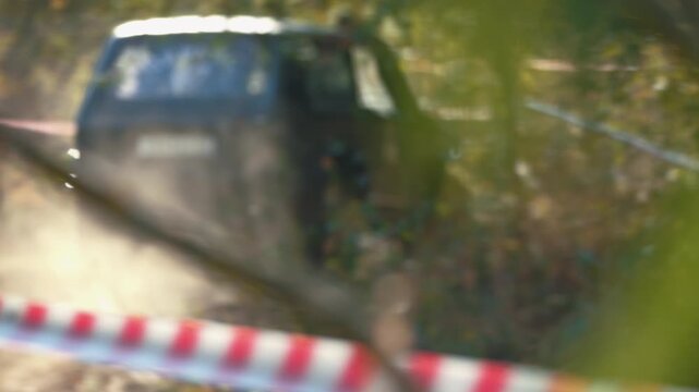 Off road car blurred in background during mud race. Red white barrier tape marks track in foreground. Shallow depth of field creates dynamic, abstract, atmospheric mood. Warm light earthy tones