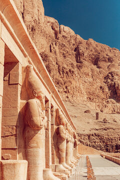 Luxor, Egypt - 04 March 2020: View of the Osiride statues at the Mortuary Temple of Hatshepsut against the backdrop of towering limestone cliffs under a clear blue sky.