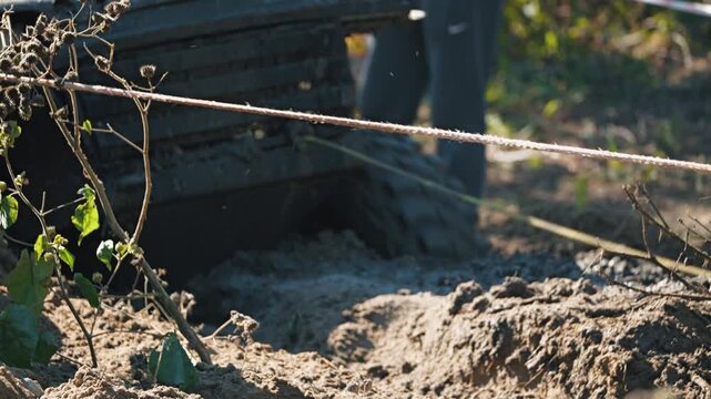 A low-angle shot of muddy terrain during an extreme off-road race. Two winch cables are in foreground, and a car stuck in deep mud is in background. A dynamic, captivating scene under bright sunlight