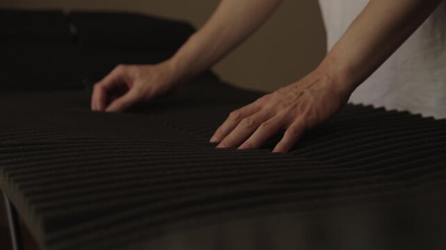 Person hands press, pinch, feel surface of black convoluted foam. Man inspects acoustic panel or mattress topper, checking material quality, texture, softness, close-up, slow motion.