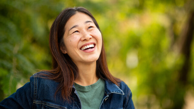 Asian woman laughing outdoors surrounded by lush green nature
