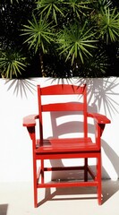 Obraz premium Bright red wooden chair sits on patio. Shadows from green plants fall on white wall. Outdoor furniture adds color and contrast to empty space. Sunny day.