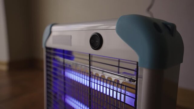 Male hand pressing switch to turn on and off electric insect killer lamp with bright ultraviolet light, modern device for pest control and protection from bugs indoors, close-up, slow motion.