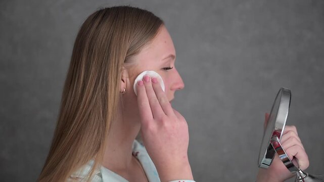 Young woman with acne-prone skin removing makeup and cleansing face with cotton pad. Daily skincare routine for problematic skin, beauty and dermatology concept.
