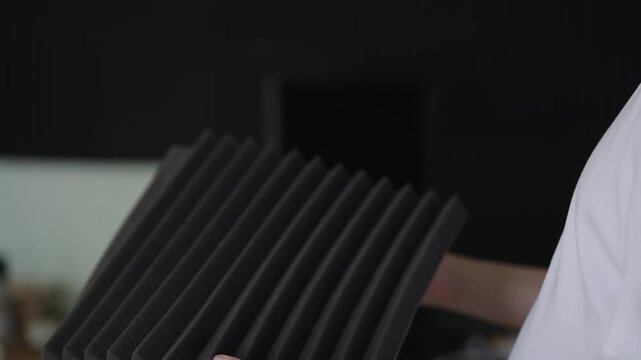 Professional sound engineer holding and folding black acoustic foam panel, demonstrating its flexibility and texture for studio sound insulation and dampening unwanted noise and echo, slow motion.