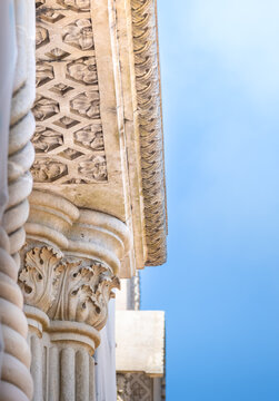 Close-up of an elegant ornamental stone column and cornice ceiling with intricate carved patterns and details against a clear blue sky.