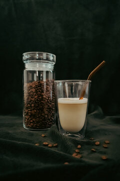 pr&eacute;sentation d'une boisson lact&eacute;e a base de caf&eacute; avec pot de caf&eacute; en grain et un verre de caf&eacute; latt&eacute; avec une paille en verre &eacute;cologique orange 