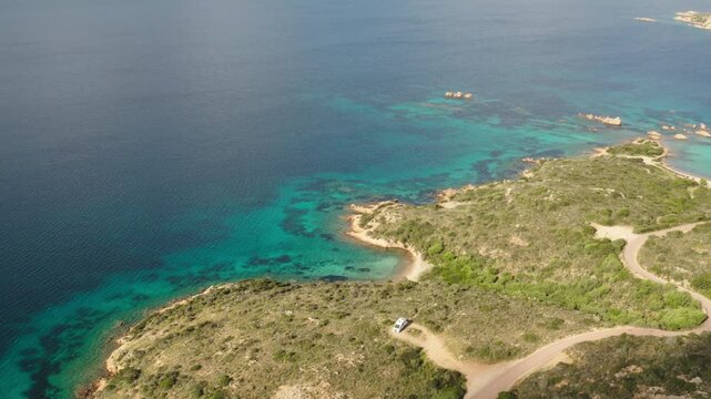 Ultra wide overhead drone shot of parked van on beautiful mediterranean island next to beach with clear turquoise blue water