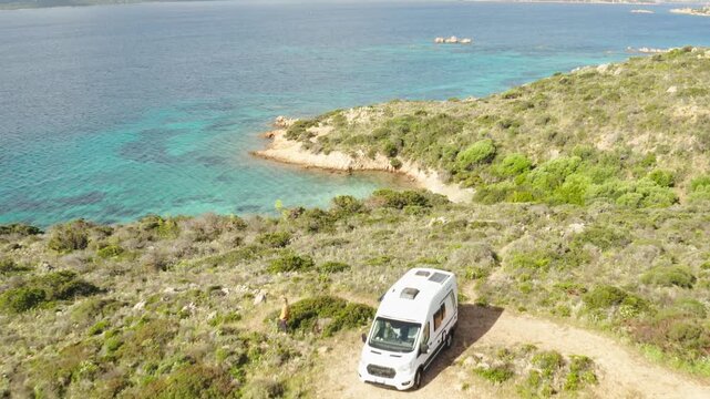 Drone flies over Camper van on mediterranean island while girl walks out to beach