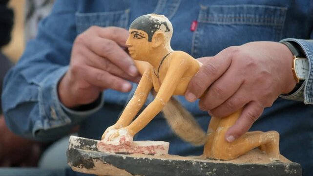 Hands of a restorer carefully brushing dust from an ancient Egyptian statuette replica
