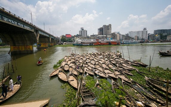 Dhaka, Bangladesh - 03 June 2026: View of numerous wooden boats clustered on the Buriganga River near a large bridge and the city skyline under a cloudy sky.