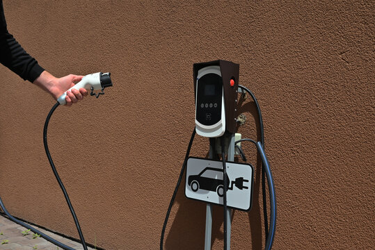 Person connecting charging cable to an electric vehicle charging station. Concept of electric mobility, renewable energy and sustainable transportation.