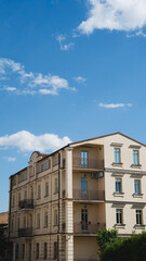 Fototapeta premium Low angle view of a classic European apartment building with beige brick facade and balconies against a bright blue sky with white clouds.
