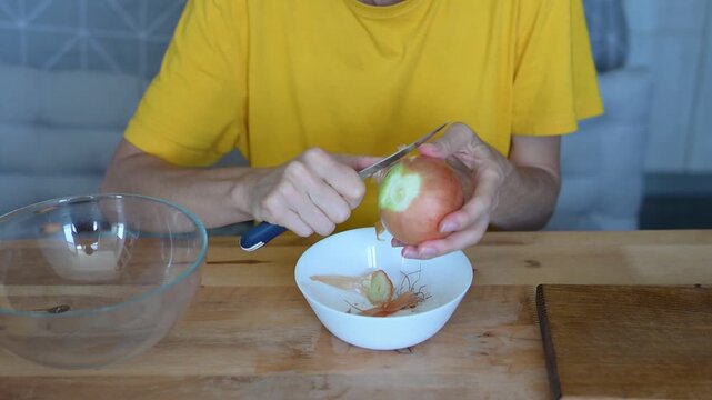 Woman holding yellow onion and preparing to peel vegetable at wooden table in home video Full HD kitchen