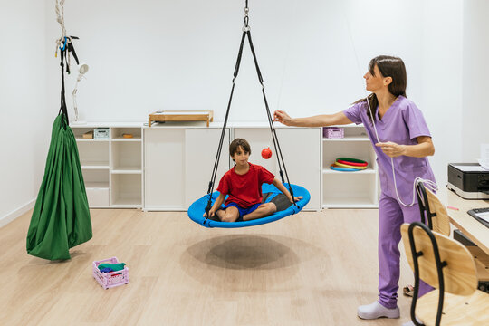 Child doing therapy exercises with occupational therapist using a swing and a ball