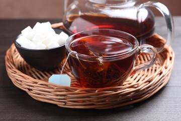 Fototapeta premium Tea bag in glass cup with hot drink, sugar and teapot on wooden table, closeup