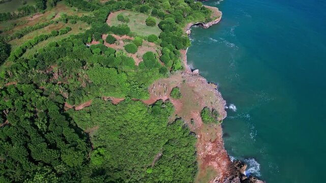 Aerial coastal cliff circular foundation ruins overlooking turquoise ocean and dense greenery, drone pans across rocky shore and round stone platform used for archaeological,Bali,Indonesia