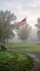 Fototapeta premium Ethereal morning scene with an American flag standing in a quiet, misty suburban park.