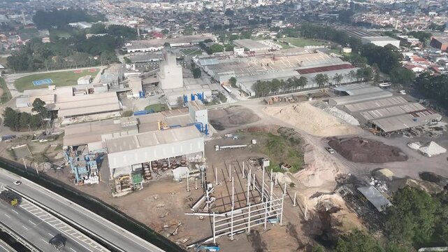 Vista superior de f&aacute;brica de materiais refrat&aacute;rios e isolantes t&eacute;rmicos, destacando galp&otilde;es, &aacute;reas de armazenamento, p&aacute;tio operacional e entorno urbano industrial.