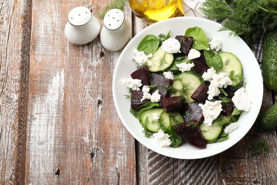 Tasty salad with boiled beet, cucumbers, feta cheese and dill on wooden table, flat lay. Space for text