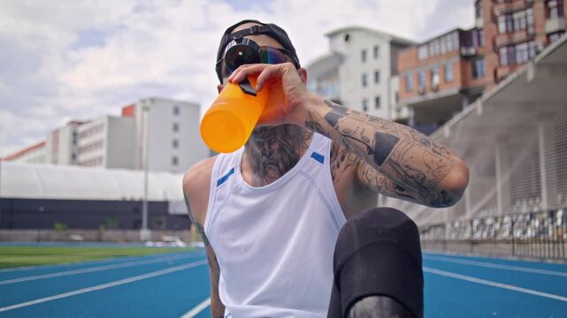Male runner with bionic prosthetic leg takes water sip on track