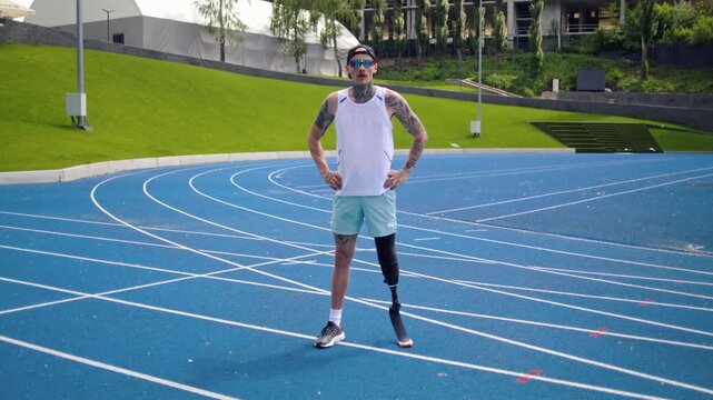 Sportsman with leg prosthesis holds hands on hips on racetrack