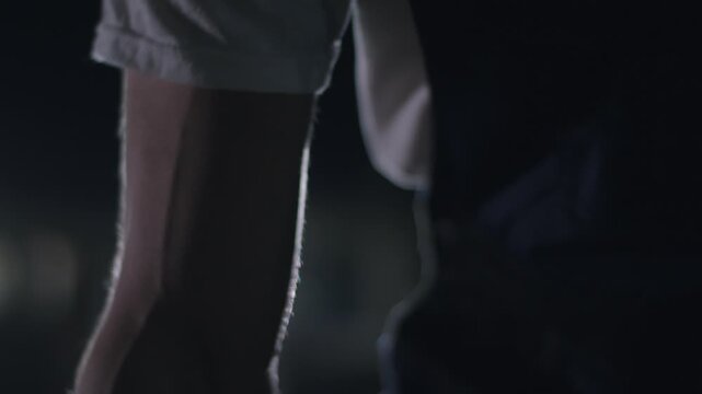 Arms tense in low light, silhouette of forearms and rolled sleeves with backlight rim, cinematic pause conveying preparation