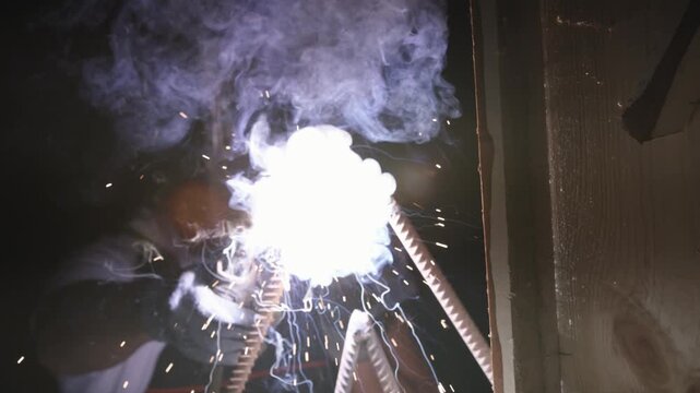 Closeup artisan welding metal sculpture with sparks, intense arc flash and blue smoke in studio setting, sparks cascading