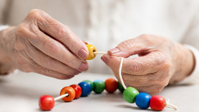 Senior woman hands stringing colorful wooden beads on rope. Rehabilitation exercise for fine motor skill development and brain training. Elderly therapy and hand coordination activity.
