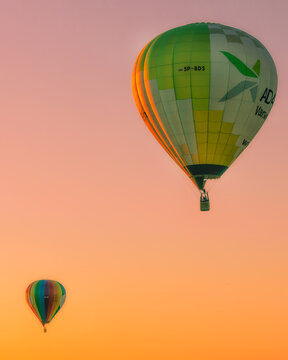 Poland - 07 August 2018: View of two hot air balloons floating in a vibrant orange and pink sunset sky over the Masovian Voivodeship region.