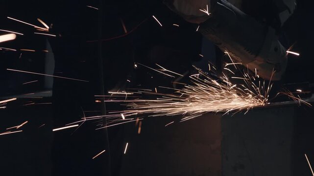 Closeup dark workshop sparks fly from grinder, dramatic metal grinding in low light with glowing embers and abrasive disc creating